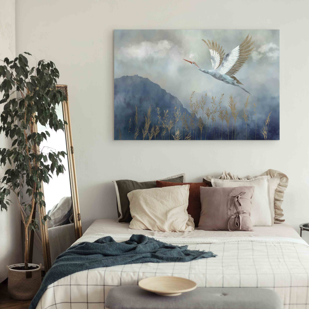 Schilderij  Vogels: A Heron In Flight - A Bird Flying Against The Background Of Dark Blue Mountains Covered With Fog